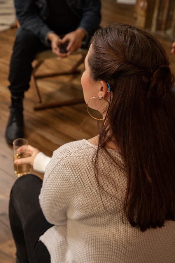 Female with a glass of wine in her hand talking with friends wearing hearing technology.