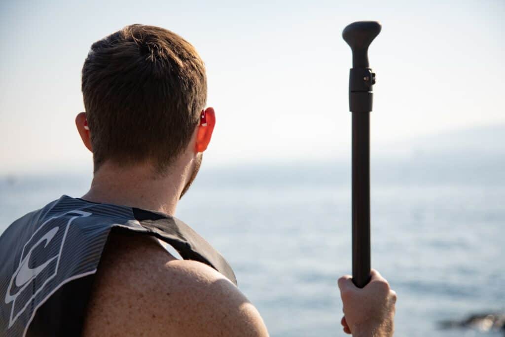 Man wearing red hearing aids and a life jacket getting ready to paddle board.