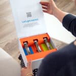 A woman holding her brightly colored hearing technology home trial. experience box with three sets of premium hearing technology.