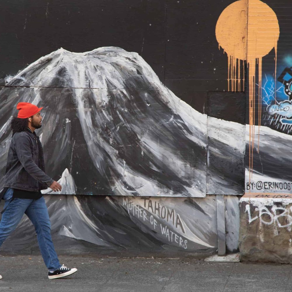 Man walking by graphite wall wearing hearing aid and looking confident.