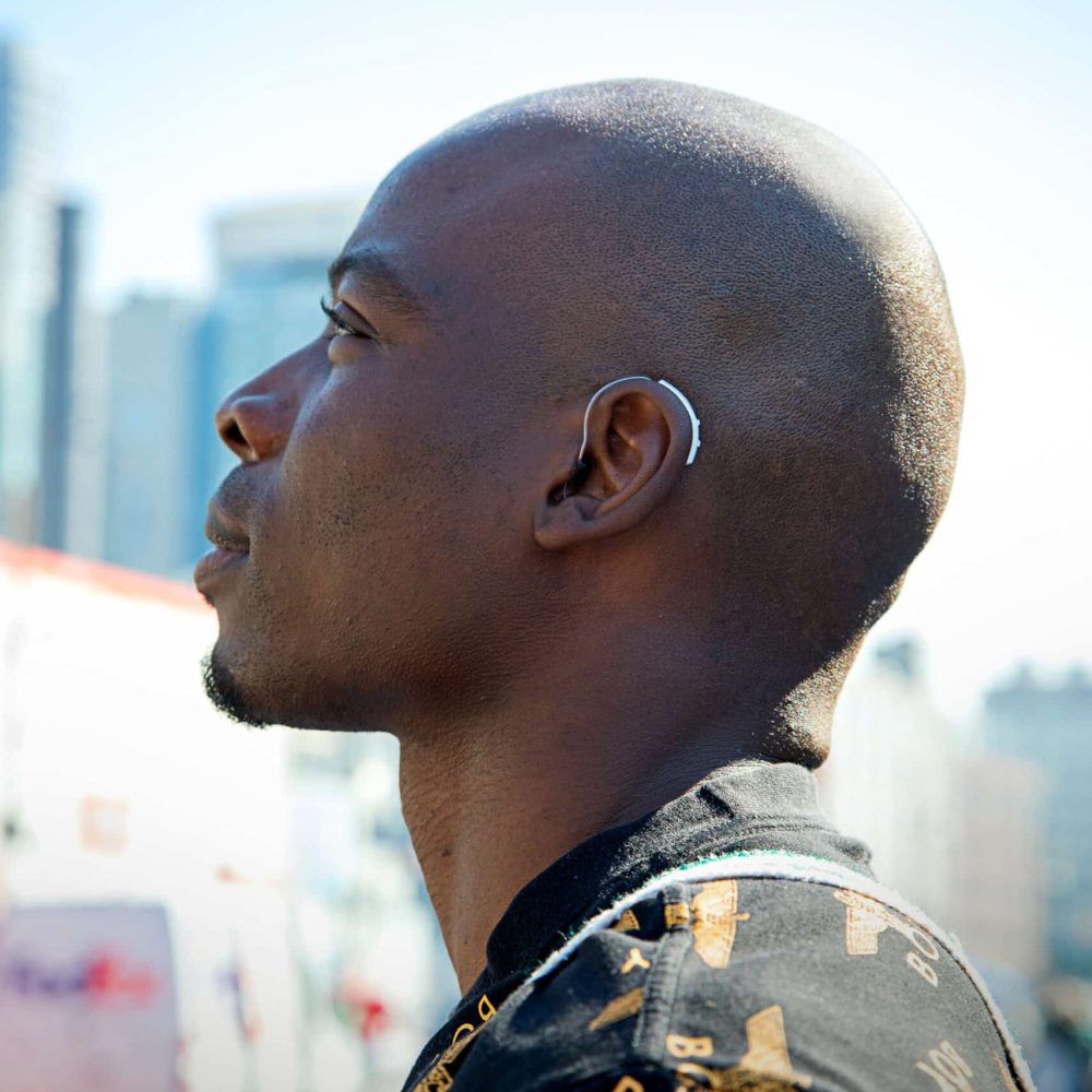 Man outdoors seen from the side wearing a sleek and discreet hearing aid.