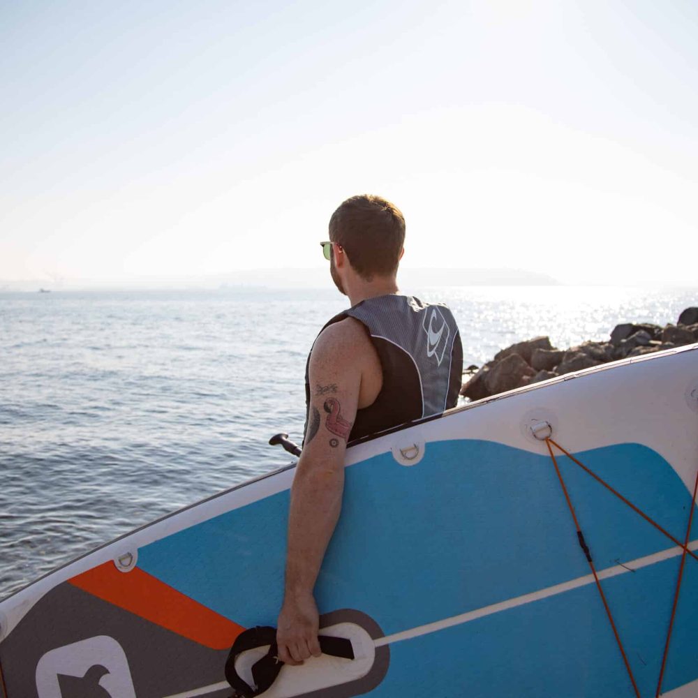 Man with surf board wearing hearing aids and looking at the ocean.